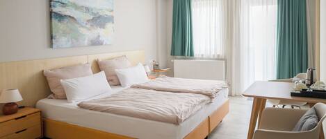 A hotel room with a bed, bedside table, lamp, and a painting on the wall.
