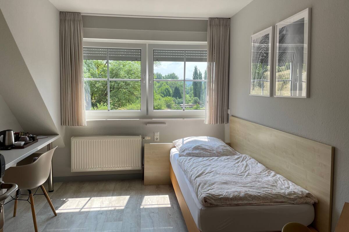 A bedroom with a bed, a desk, a chair, a radiator, and a window with curtains.
