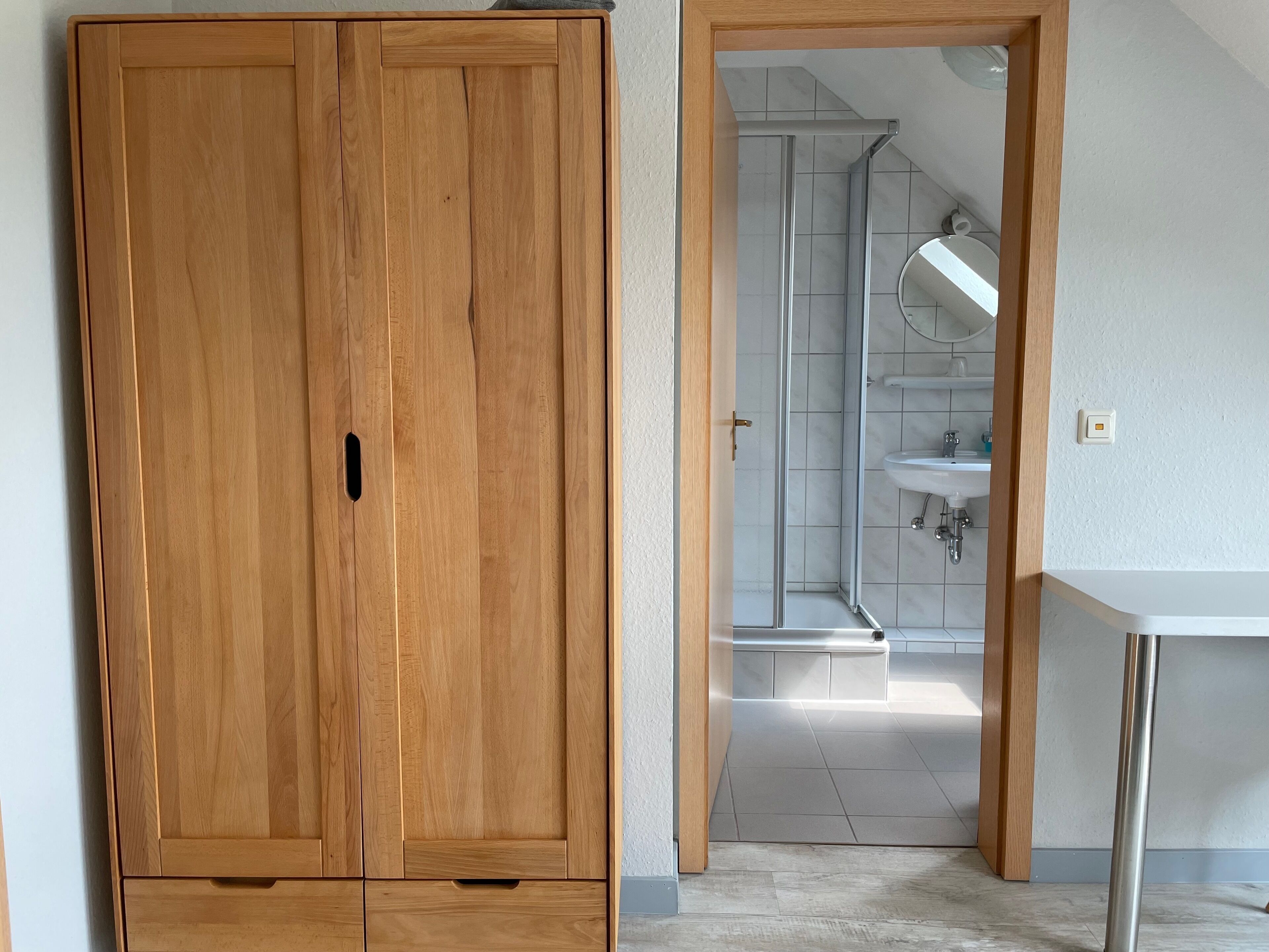 Un armadio in legno, un bagno con doccia e un lavandino bianco.