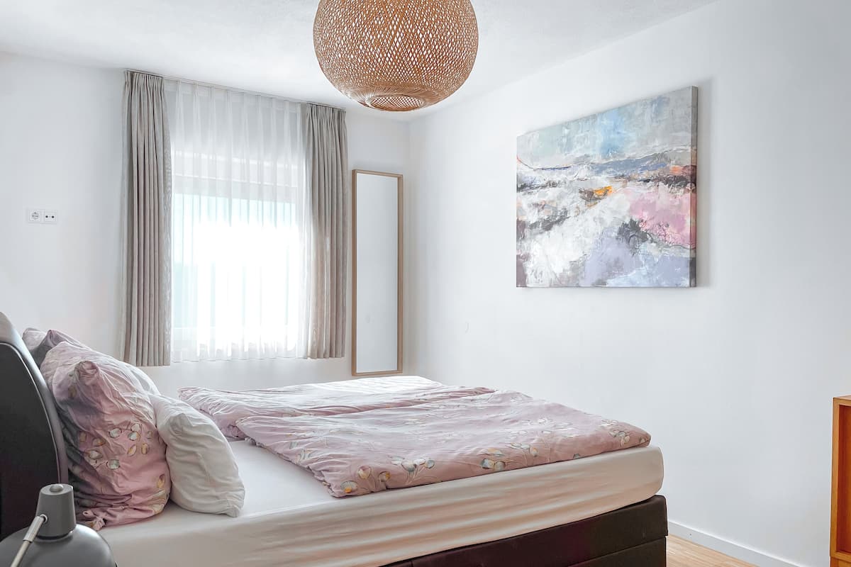 A bedroom with a bed, a bedside table, a lamp, a mirror, and a painting on the wall.