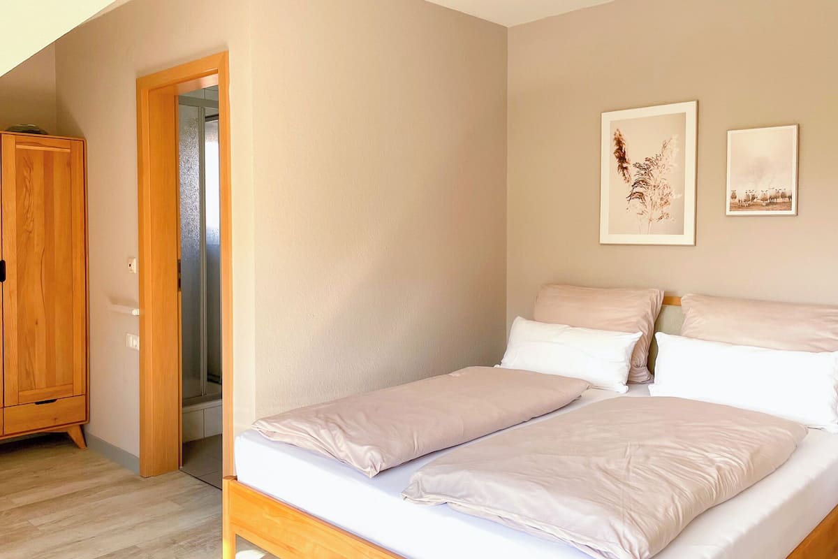 A bedroom with a bed, a wooden wardrobe, and two framed pictures on the wall.