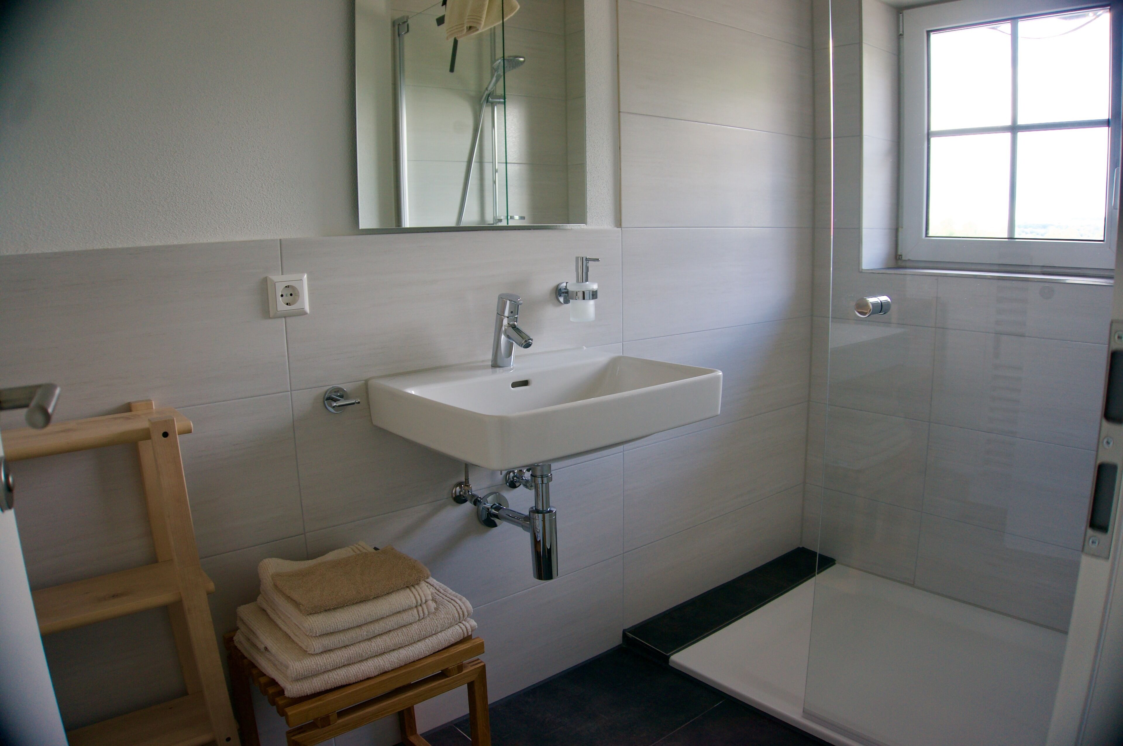A bathroom with a white sink, a mirror, a shower, and a window.