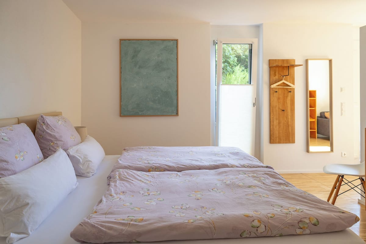 A bedroom with a bed, a window, a mirror, and a door.