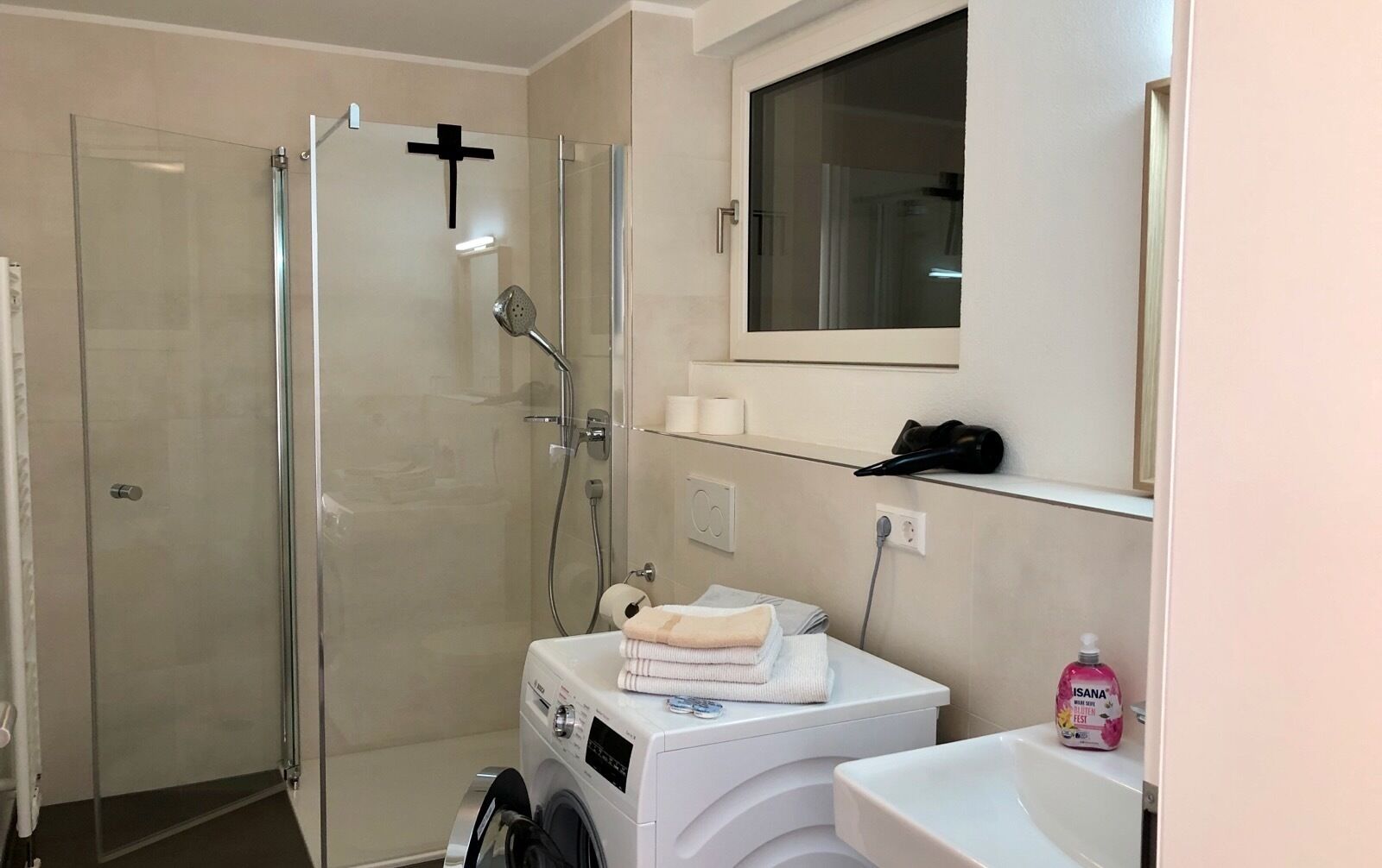 A bathroom with a glass-enclosed shower, a washing machine, a sink, and a mirror above the mirror cabinet.