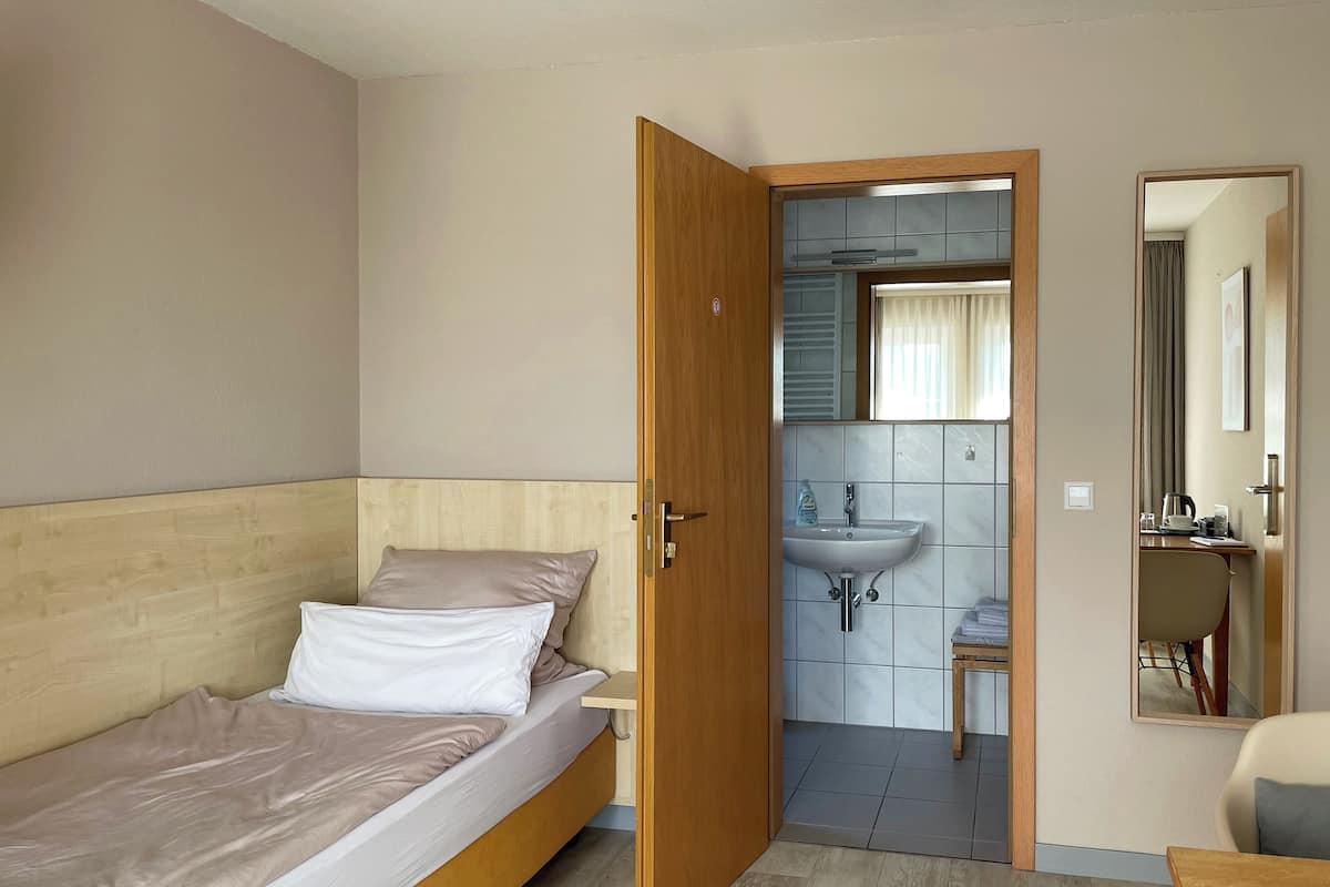 A bedroom with a bed, a wooden door leading to a bathroom with a sink and mirror.