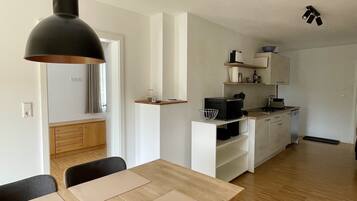 Une cuisine moderne avec des meubles blancs, une table à manger en bois et un luminaire suspendu noir.