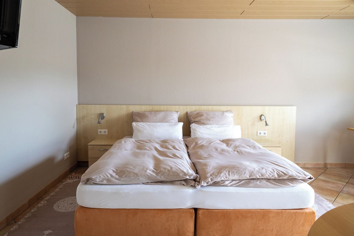 A double bed with two pillows, a wooden headboard, a bedside table, and a nightstand.