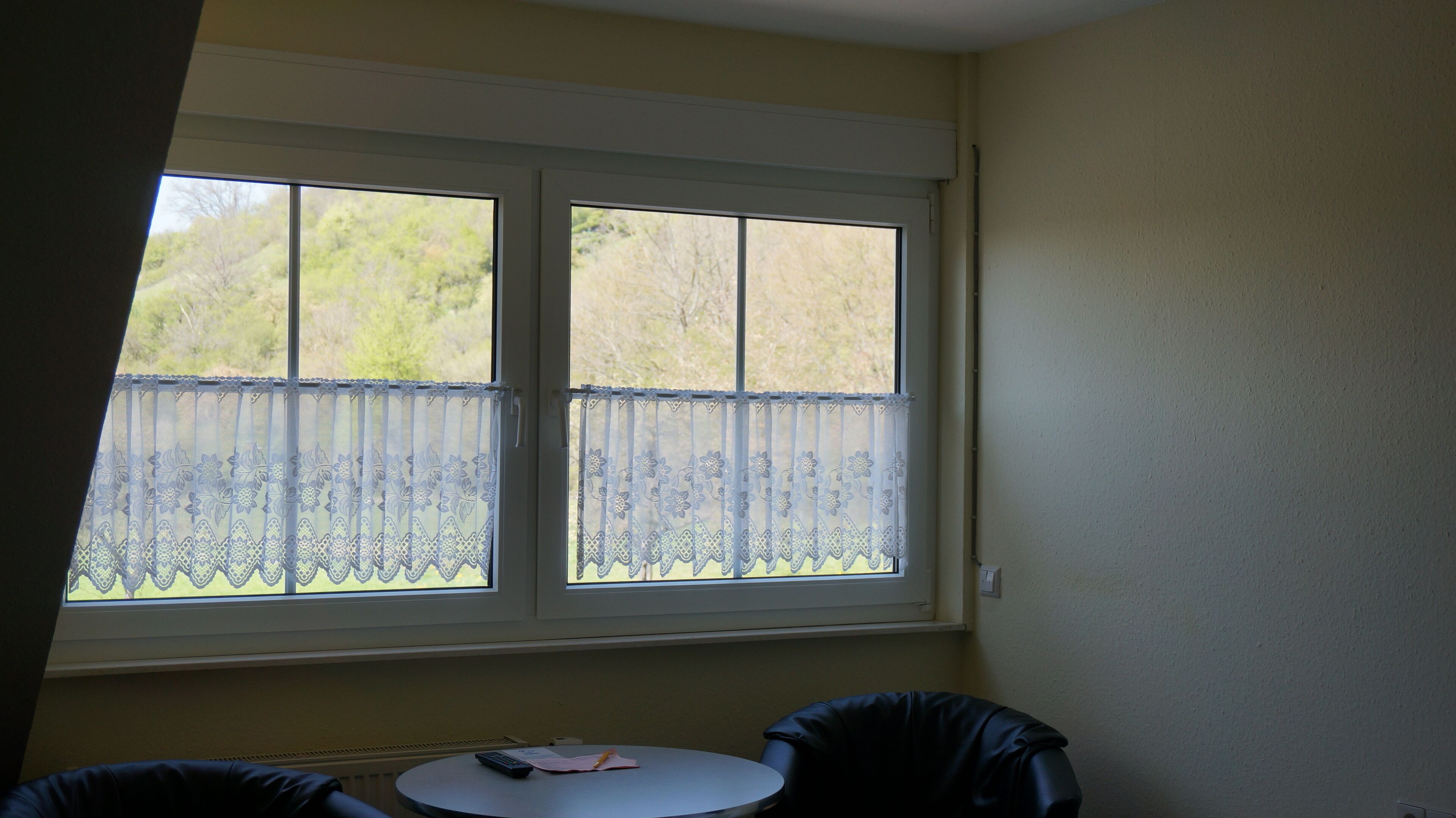 A room with a large window, a small round table, and a chair.
