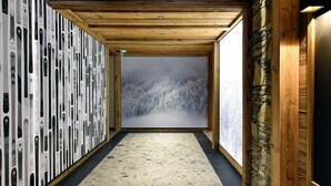 A hallway with a wooden ceiling, a stone wall, and a large window with a snowy forest view.