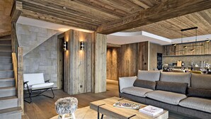 A modern living room with a wooden ceiling, a stone wall, a staircase, a sofa, a coffee table, and a small stool.