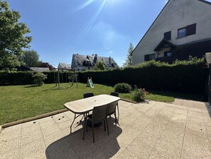Eine Terrasse mit Tisch und Stühlen, einer Schaukel und einer Rutsche im Garten.
