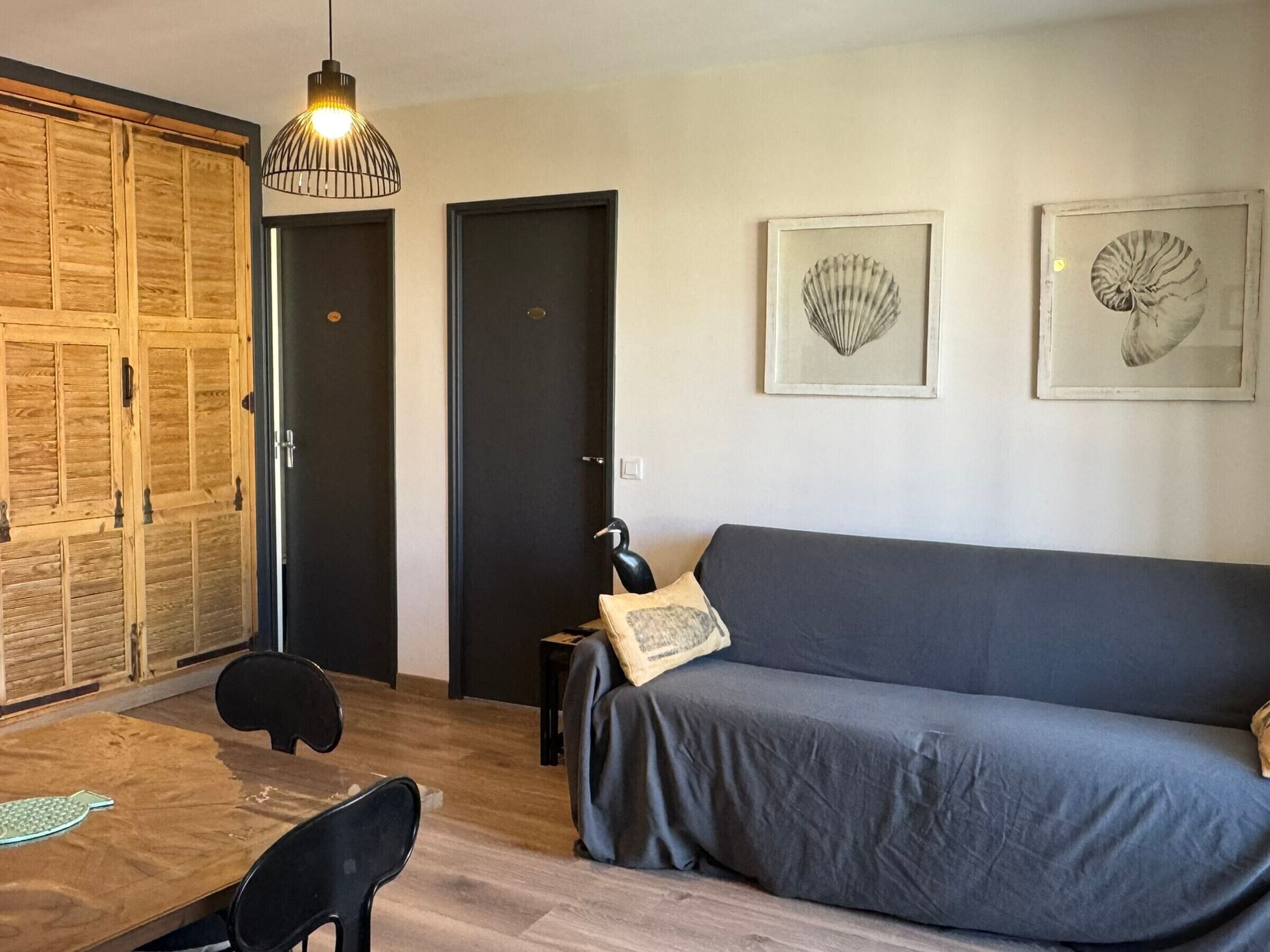 Ein modernes Wohnzimmer mit einem grauen Sofa, einem Holzschrank und zwei gerahmten Wandbildern mit Muscheln.