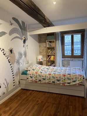 Een slaapkamer met een bed, een boekenkast, een raam met gordijnen en een muurschildering.