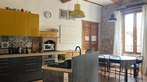 A kitchen with a microwave, oven, and various appliances. There is a dining area with a table and chairs. The kitchen has a yellow cabinet and a tiled backsplash. - In a historic 12th-century building (Montfrin)