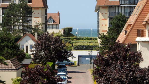 Una calle residencial con casas, cielo despejado y vista al mar.