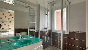 Un baño con cabina de ducha de vidrio, tocador doble y un espejo grande.