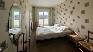 Un dormitorio con cama, una silla de madera, un espejo y una ventana.