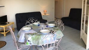 Un coin repas avec une table dressée pour quatre personnes, un canapé noir, un meuble et un téléviseur posé sur une table d’appoint.