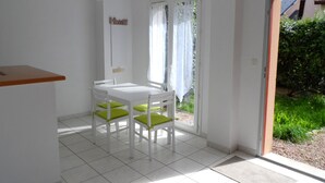 A small, bright room with a white table and chairs, a door leading outside, and a 'Home' sign on the wall. - Charming 3-Room Cottage with Private Garden, Near Marina, Sleeps 6, Pet-Friendly, Pool Access (Dives-sur-Mer)