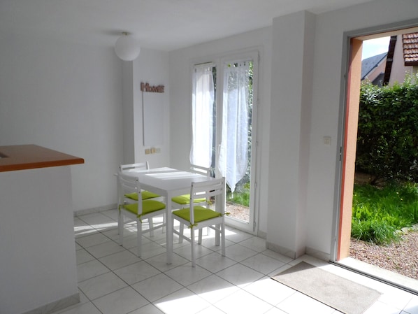 Una habitación pequeña y luminosa con una mesa y sillas blancas, una puerta que da al exterior y un letrero que dice 'Home' en la pared.