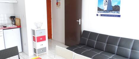 Una habitación con sofá, mesa de comedor, zona de cocina y un cartel en la pared.