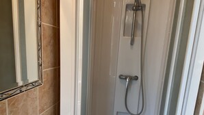 Ducha con puerta de vidrio, espejo y pared de azulejos.