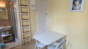 Una habitación pequeña y limpia con una mesa y sillas blancas, un lavabo blanco y una escalera apoyada en la pared.