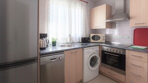 Une cuisine moderne équipée d’appareils électroménagers en acier inoxydable, d’un lave-vaisselle, d’une machine à laver et de meubles de rangement en bois.