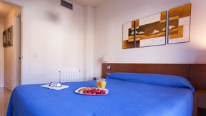 Une chambre d’hôtel avec un lit, une table de chevet, une lampe fixée au mur et un tableau.