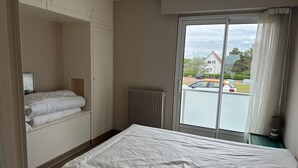 A hotel room with a bed, a radiator, a window with a view of the outside, and a wardrobe. - Stunning Sea View Apartment in Varaville – Beachfront Loggia, Sleeps 4 (Le Home Varaville)