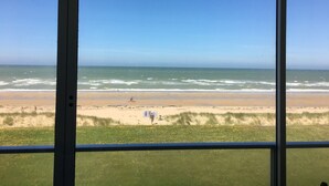 A view of a beach through a window, with the ocean and sandy shore visible. - Stunning Sea View Apartment in Varaville – Beachfront Loggia, Sleeps 4 (Le Home Varaville)