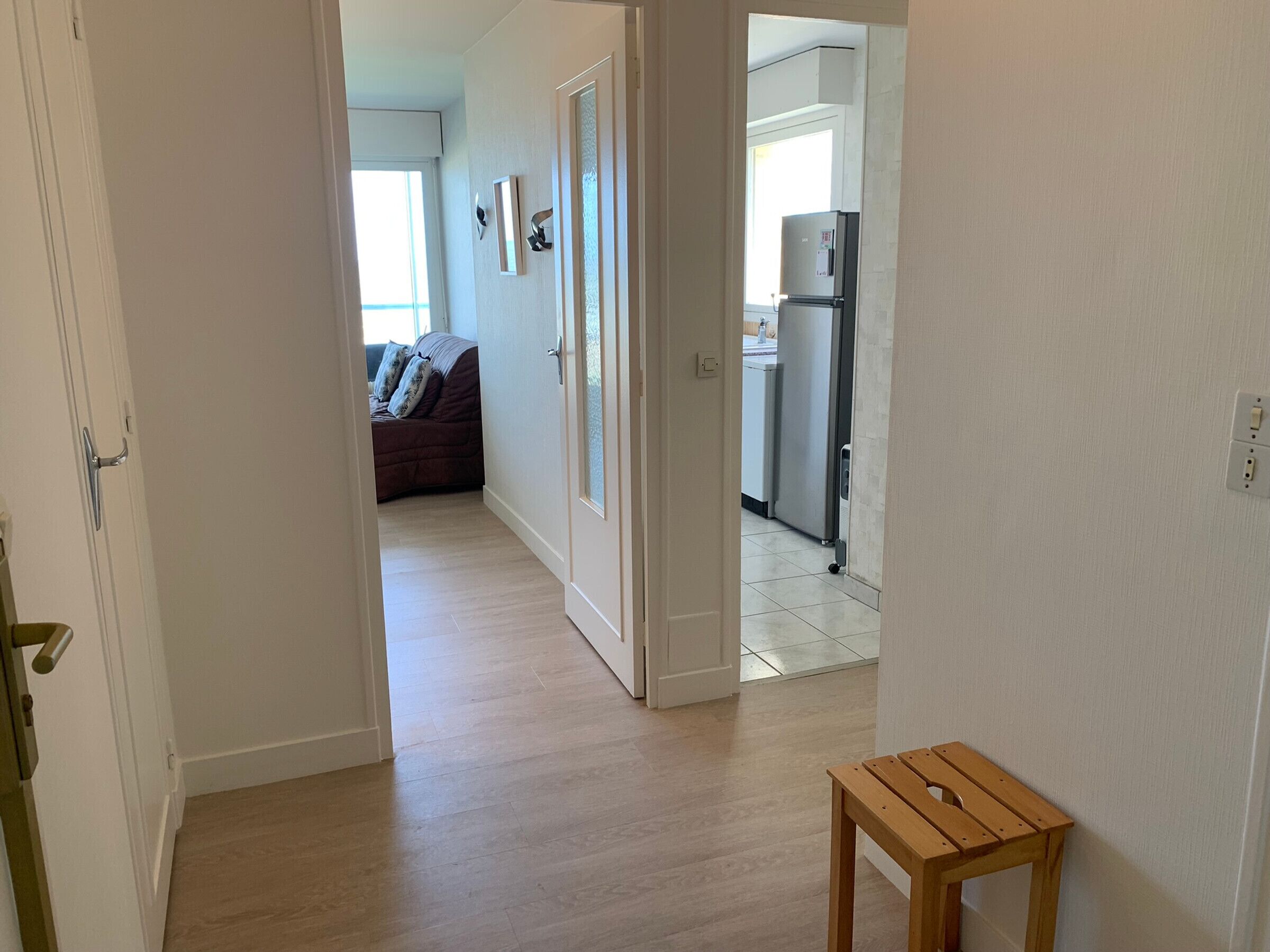 Un couloir avec une table en bois, un canapé et un coin cuisine équipé d’un réfrigérateur.