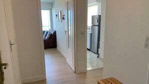 A hallway with a wooden table, a sofa, and a kitchen area with a refrigerator. - Stunning Sea View Apartment in Varaville – Beachfront Loggia, Sleeps 4 (Le Home Varaville)