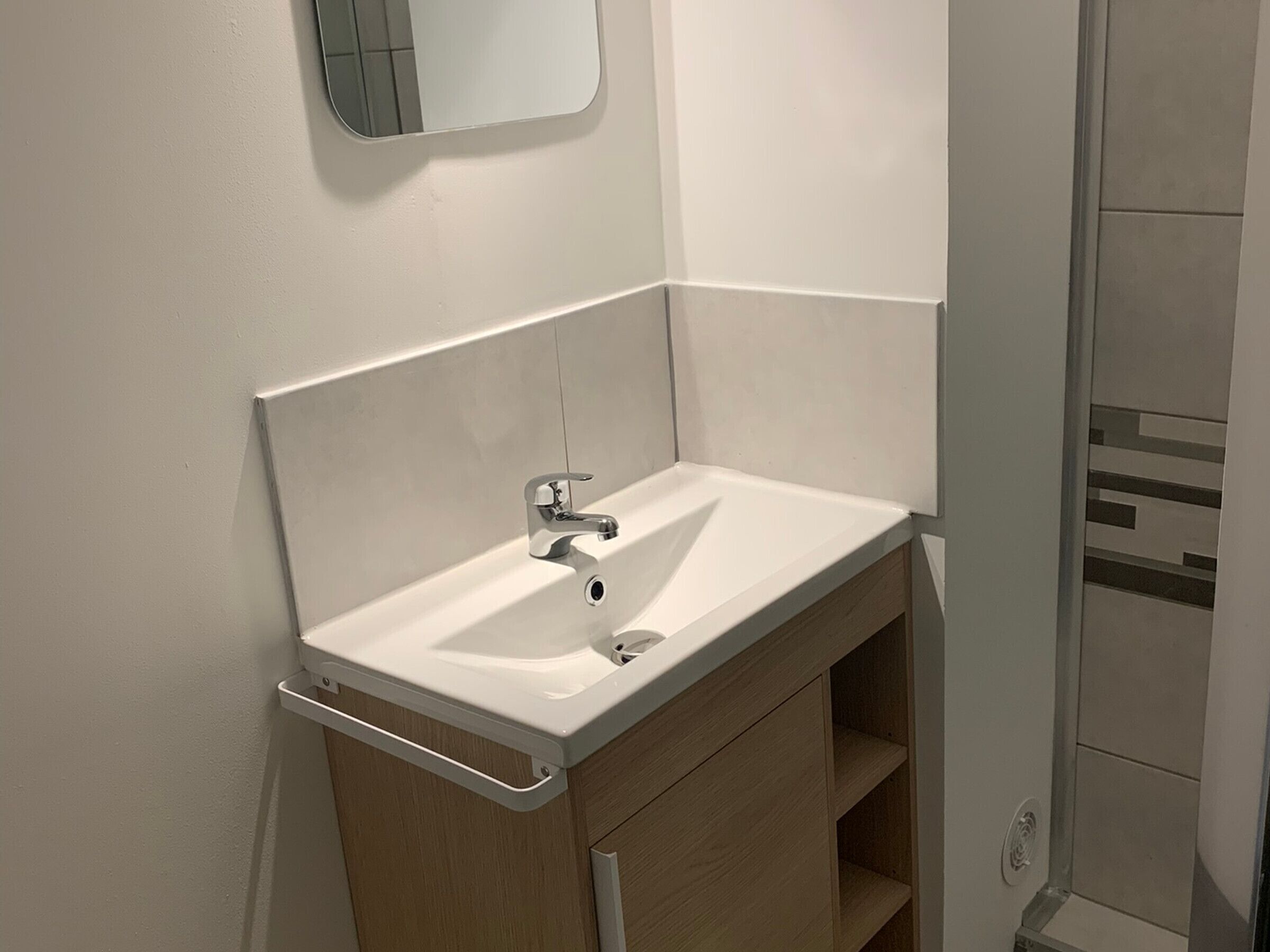 A bathroom with a white sink, a mirror above it, and a wooden cabinet below.
