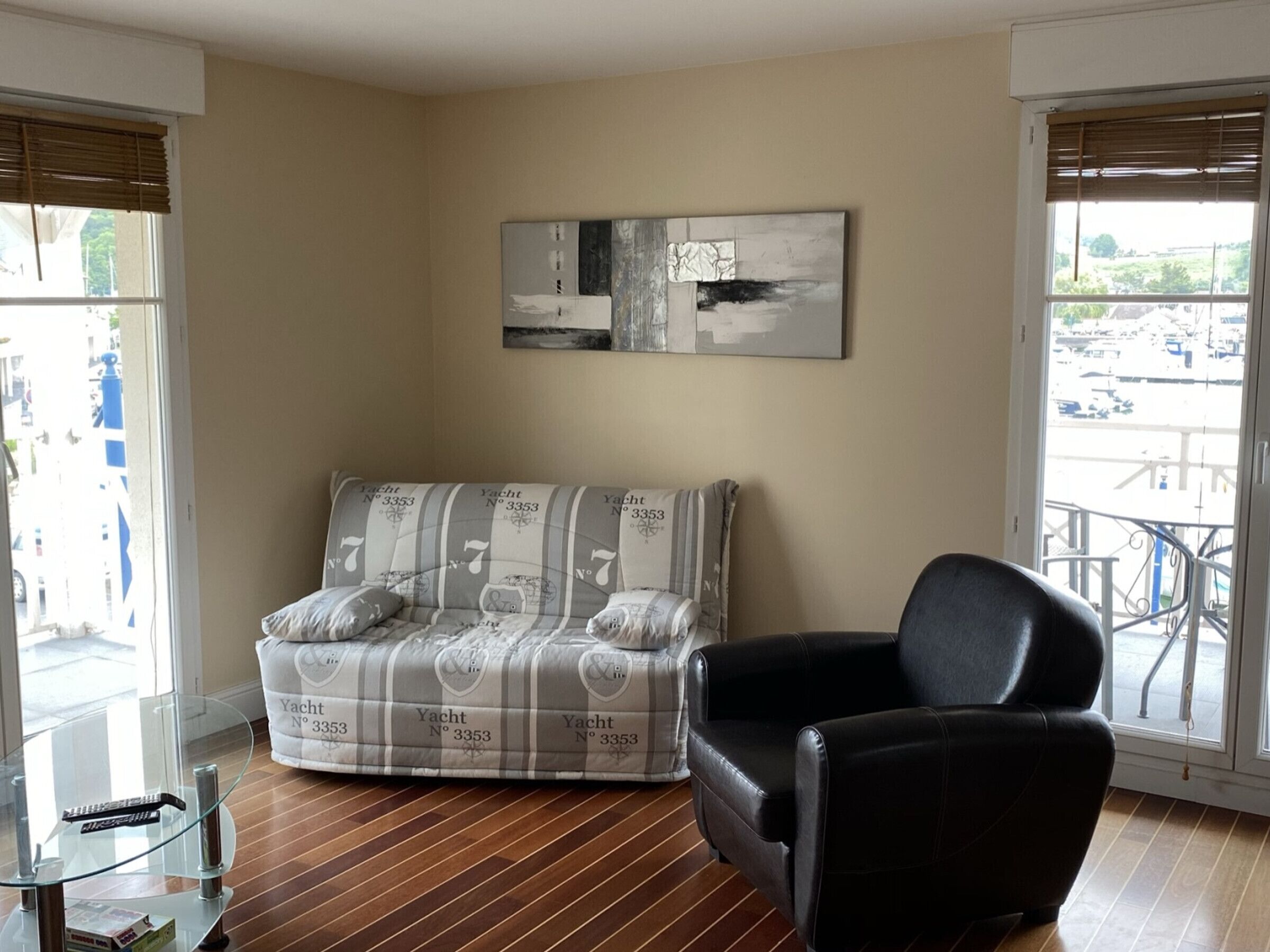 A living room with a sofa, a black armchair, a glass coffee table, and a painting on the wall.