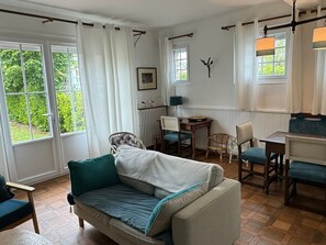A cozy room with a sofa, chairs, a dining table, and a view of greenery outside.