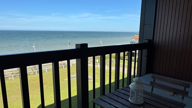 Ein Balkon mit Blick auf das Meer, einem Holztisch und einem weißen Laternen.