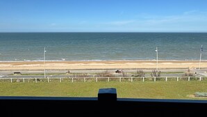 Blick auf die Küste vom Balkon mit Strand, einer Straße, einem Fahrrad und einem Zaun.