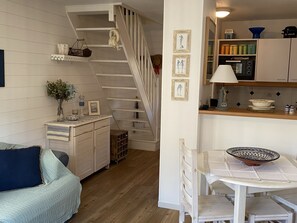 A cozy kitchen with a wooden staircase, a dining table with a bowl, and a small seating area with a couch.