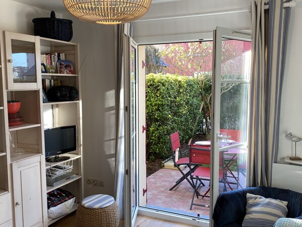 A room with a sliding glass door leading to a patio with a table and chairs, a bookshelf, a television, and a sofa.