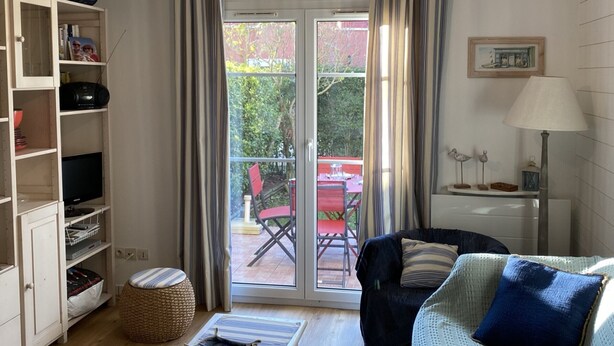 Uma sala de estar com sofá, poltrona, mesa, luminária, estante de livros e uma janela grande com cortinas.