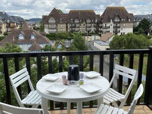 Un balcón con una mesa redonda y sillas blancas, con vista a una hilera de casas tradicionales con tejados inclinados.