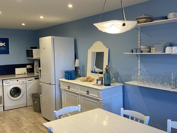 A compact kitchen with a washing machine, a refrigerator, a dining table with chairs, and a hanging light fixture. - Spacious 4-Room Duplex with Sea View: TV, Internet, Pet-Friendly - Cabourg, France (Cabourg)