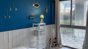 Un dormitorio con pared azul, cama blanca y ventana con vistas al exterior.