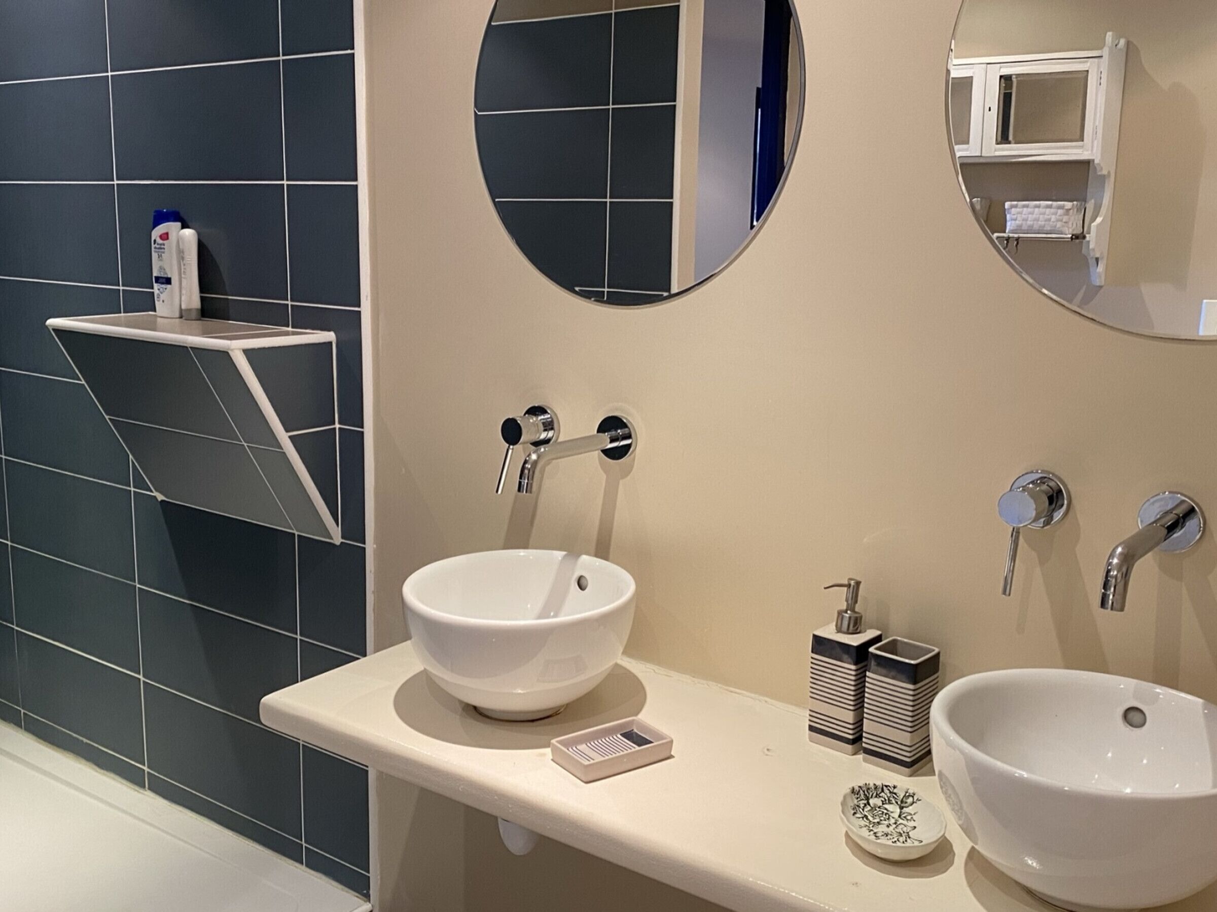 A modern bathroom with two white sinks, a mirror, and a shelf with toiletries.