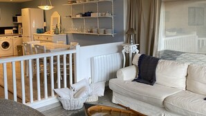 Una sala de estar moderna con un sofá blanco, un comedor con mesa y sillas, una cocina equipada y un área de lavandería.