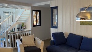 Una sala de estar con una escalera, un sofá azul, un sillón blanco y un cuadro enmarcado en la pared.