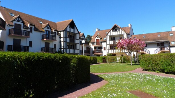 A row of traditional half-timbered houses with balconies, a well-maintained garden, and a clear blue sky. - Duplex 3-Room Apartment Near Beach in Cabourg - Sleeps 6, Parking Included (Le Home Varaville)
