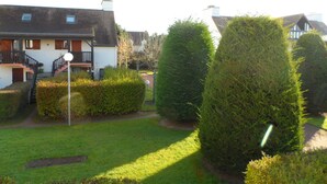 A residential area with a well-maintained lawn, neatly trimmed hedges, and a house with a visible staircase and windows. - Duplex 3-Room Apartment Near Beach in Cabourg - Sleeps 6, Parking Included (Le Home Varaville)