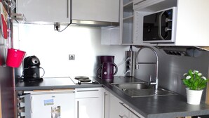 Una cocina compacta con microondas, cafetera y un lavamanos pequeño.